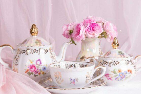 a teapot and teacup next to a vase of pink roses