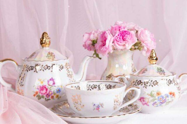 a teapot and teacup next to a vase of pink roses