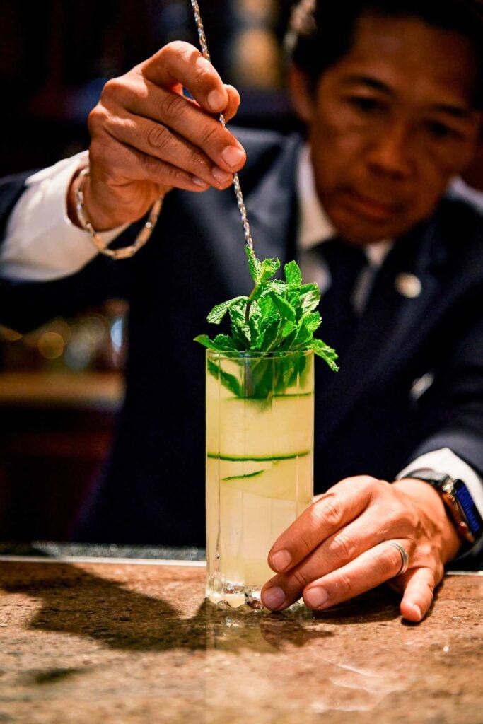 bartender pushing mint into a cocktail in a hiball