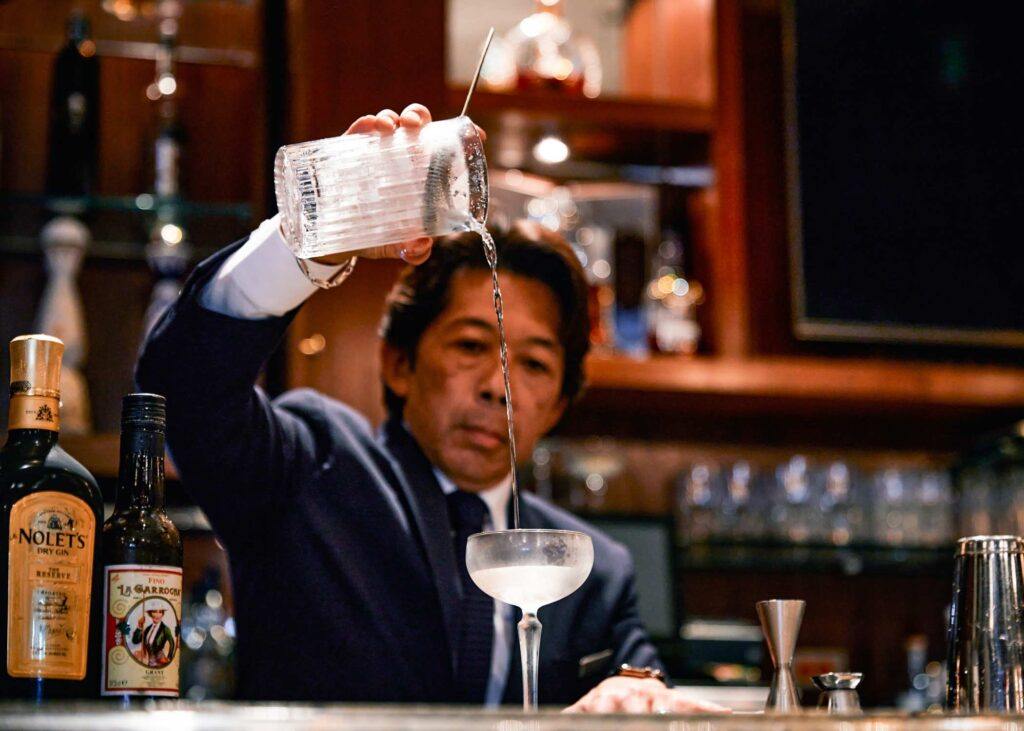bartender straining a cocktail into a chilled glass
