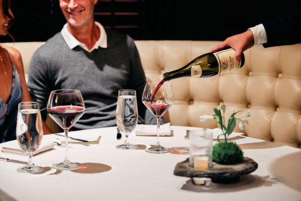 a couple sitting at a table while red wine is being poured