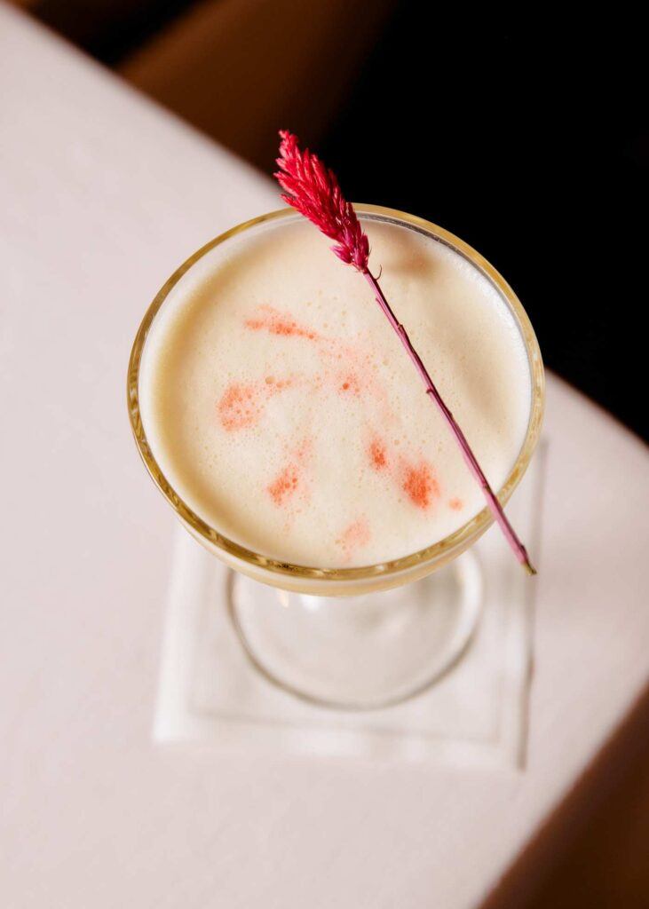 a frothy cocktail with a colored grass stem across the rim