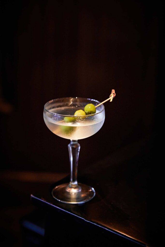 a clear cocktail with 3 olives speared on a tooth pick