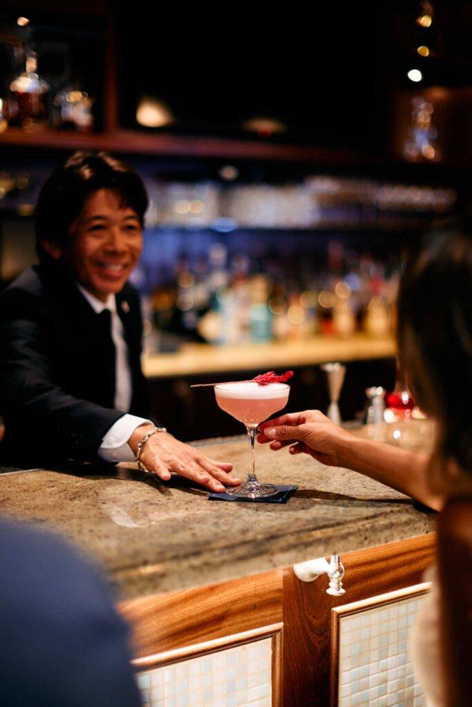 bartender handing customer a pink, frothy cocktail