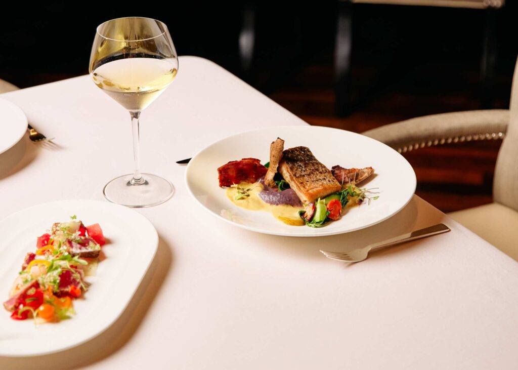 a plate of food with a side serving of vegetables and a glass of white wine