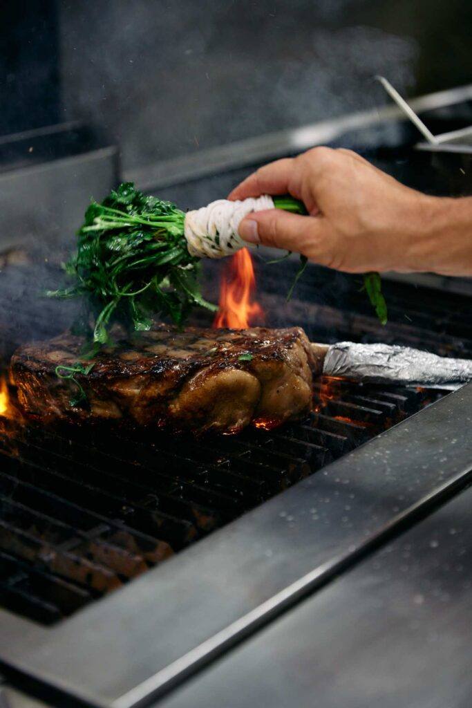 chef basting a grilling steak with a herb brush