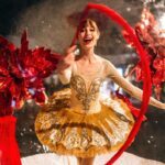 a ballerina in a gold dress twirling a red ribbon
