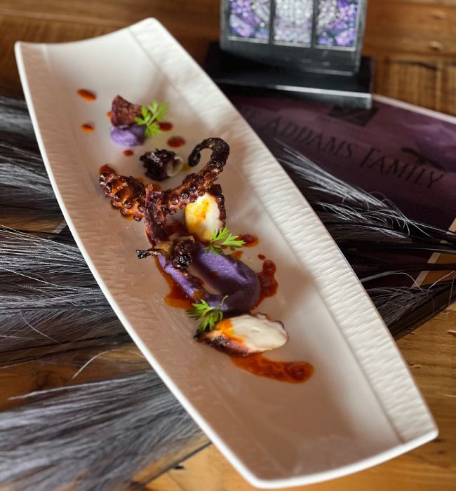 grilled octopus, purple puree, and spooky decor featuring a skull lantern.