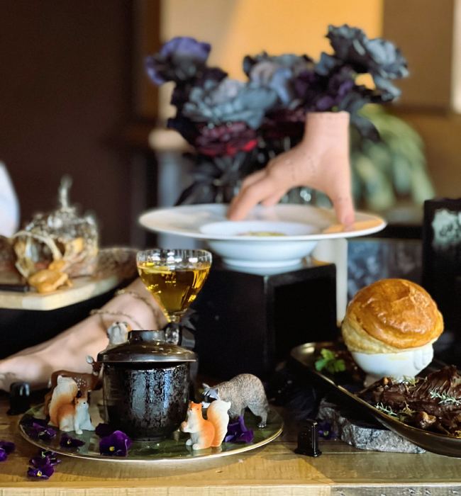 Spooky Halloween table with fake hand, dark flowers, and eerie food setup.