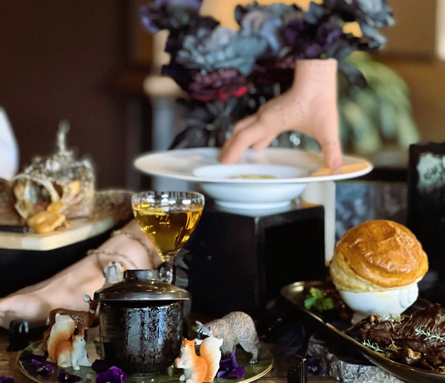 Spooky Halloween table with fake hand, dark flowers, and eerie food setup.